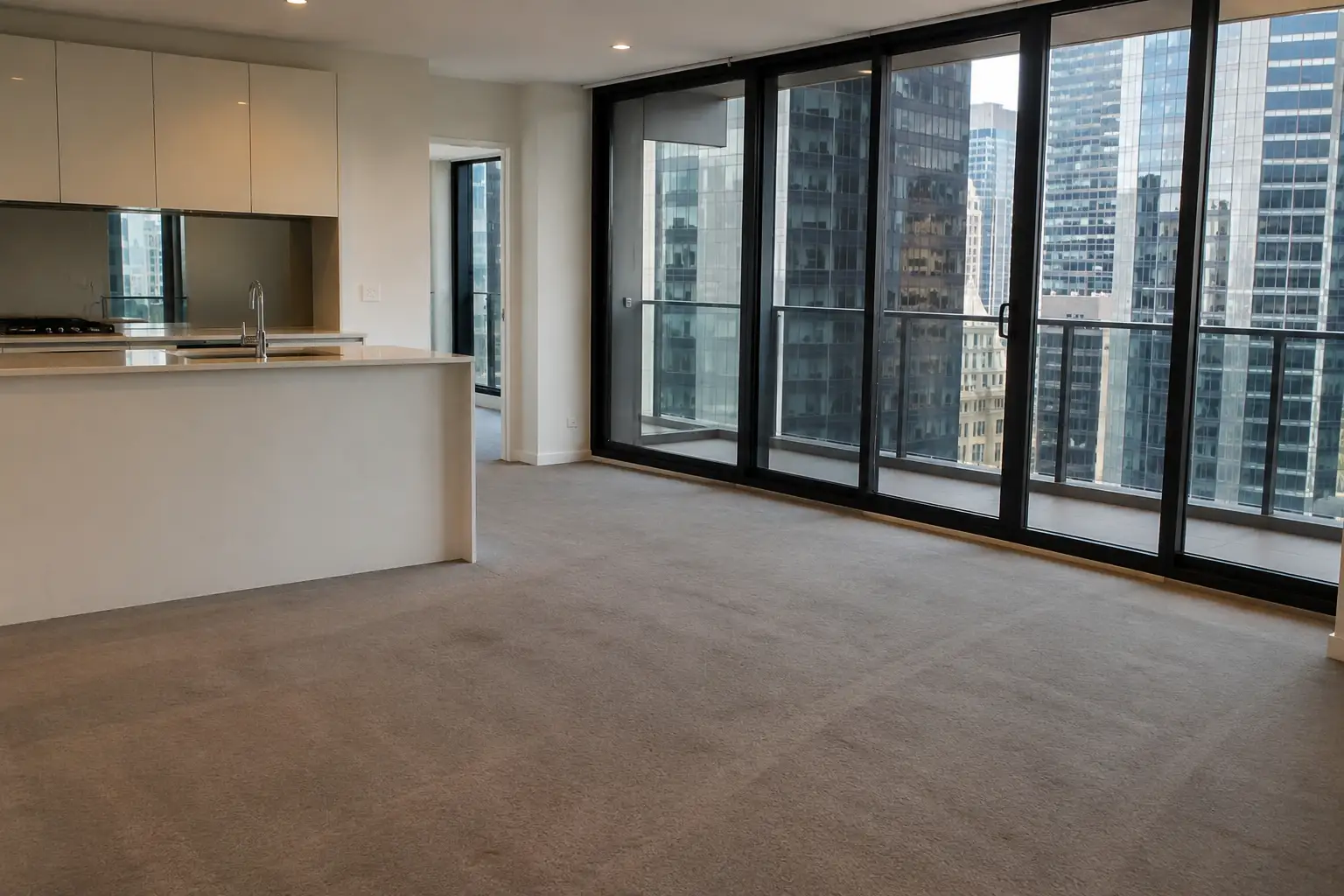 Empty Melbourne CBD apartment after end of lease cleaning with spotless carpets, polished kitchen surfaces, floor-to-ceiling windows, and panoramic city skyline views, professionally prepared for final property inspection.
