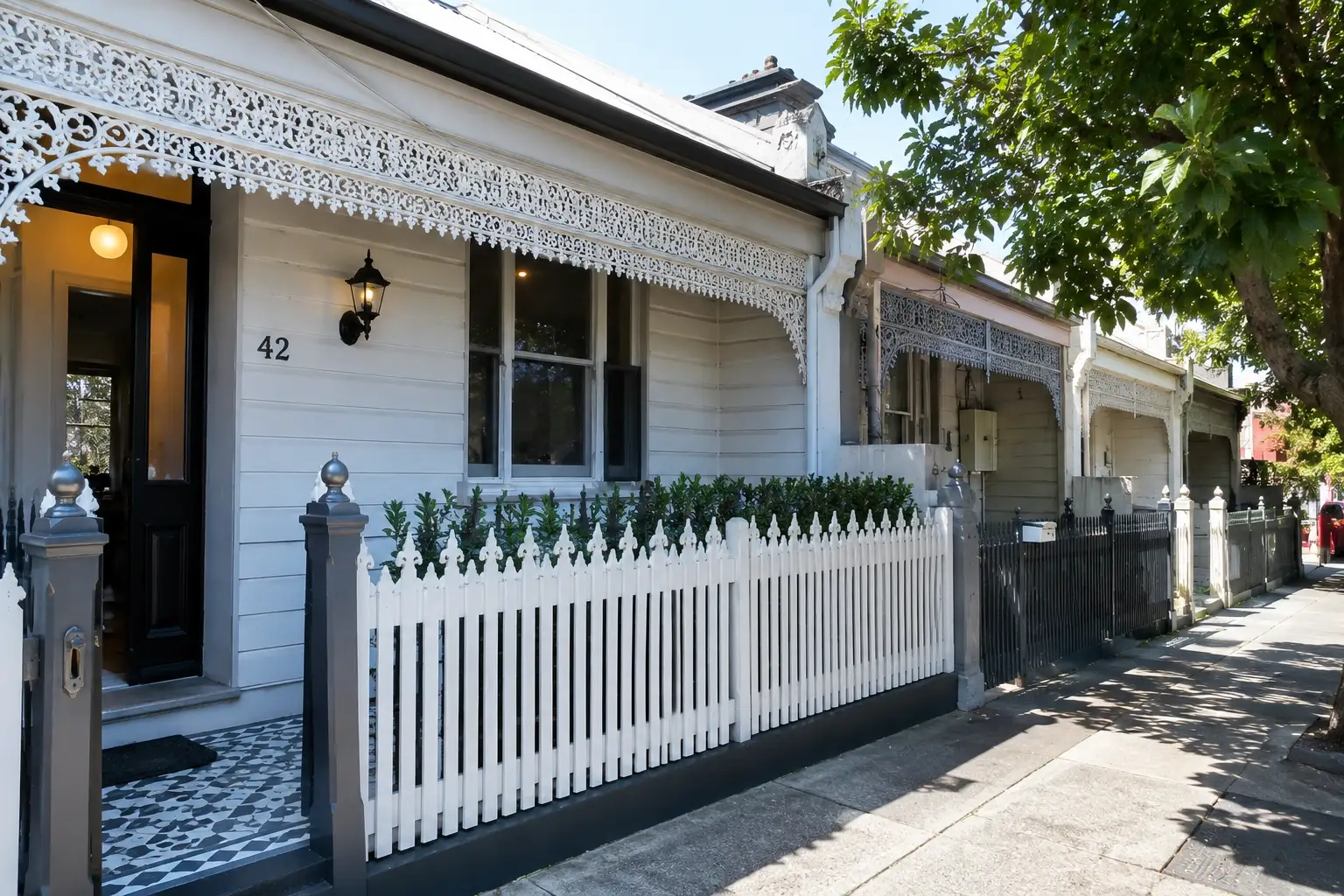 Victorian timber cottages in Port Melbourne with heritage weatherboard façades, ornate lacework verandas, white picket fences, and a quiet tree-lined residential street.