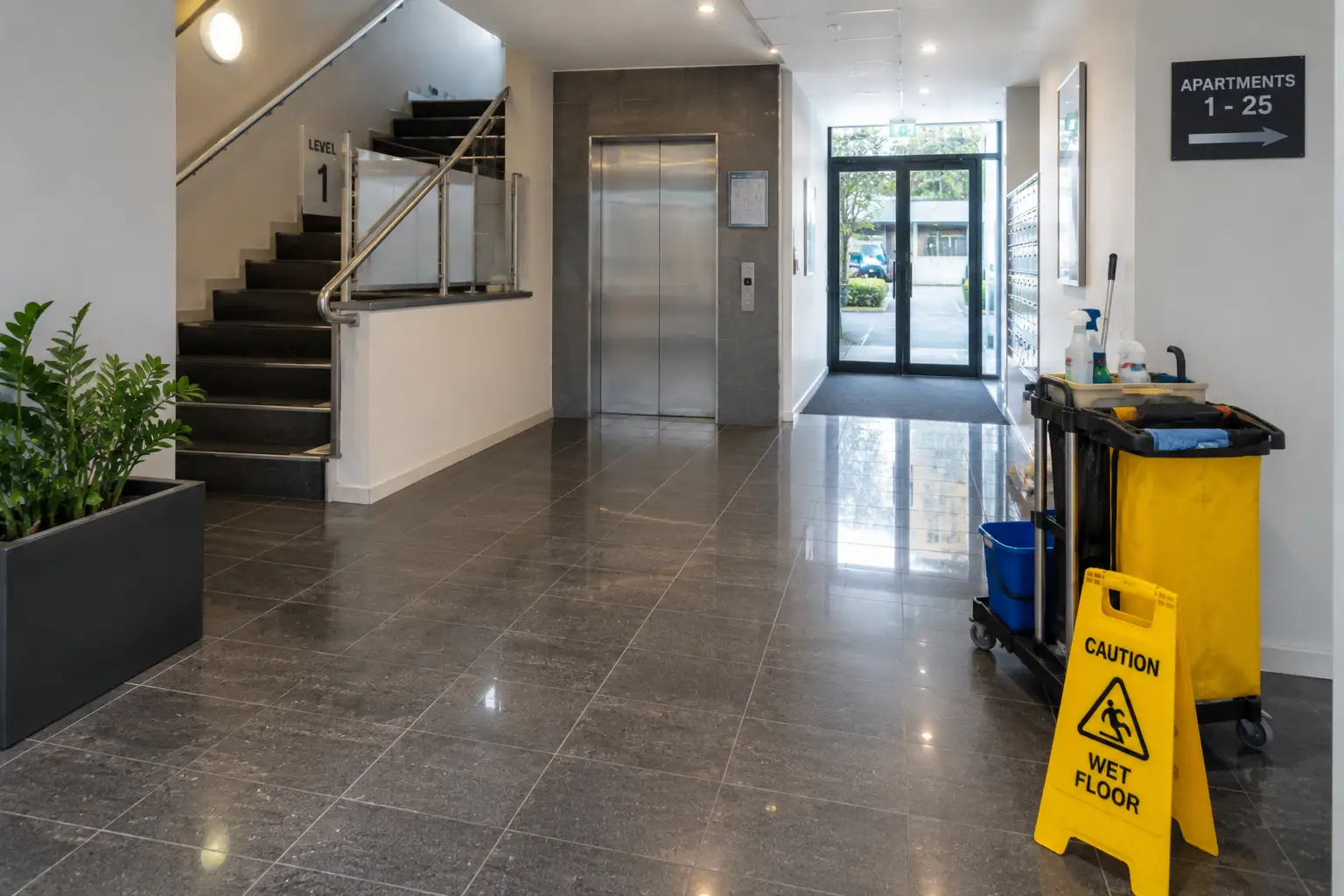 Modern apartment building lobby with polished floors, elevator, stairs, entrance area and professional cleaning equipment, representing strata cleaning in Dandenong.